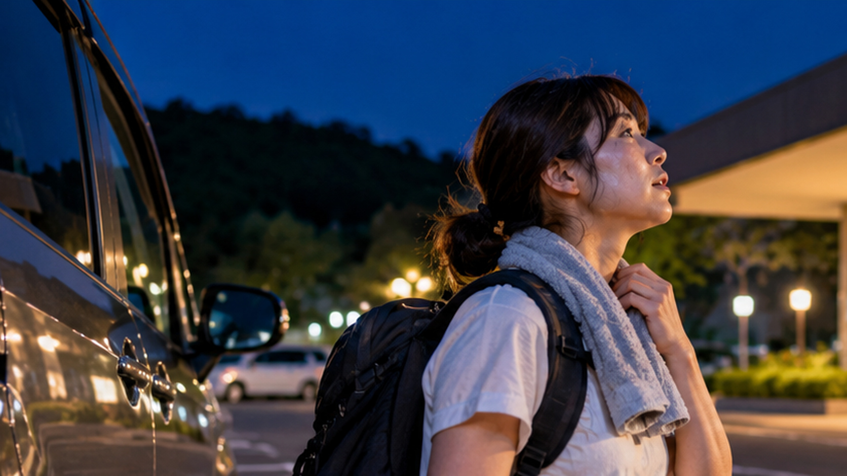 夏の夜、暑さで車中泊を取りやめ、停車した車のそばから宿泊施設へ向かおうとする女性